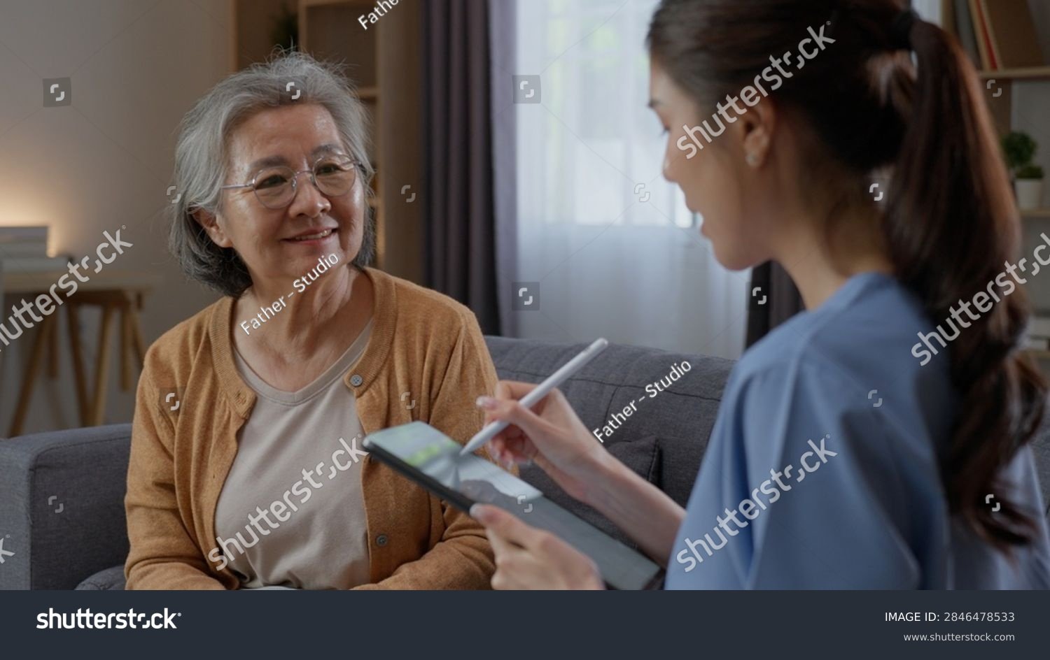 Pflegekraft erfasst Informationen auf einem Tablet neben einer aelteren Bewohnerin